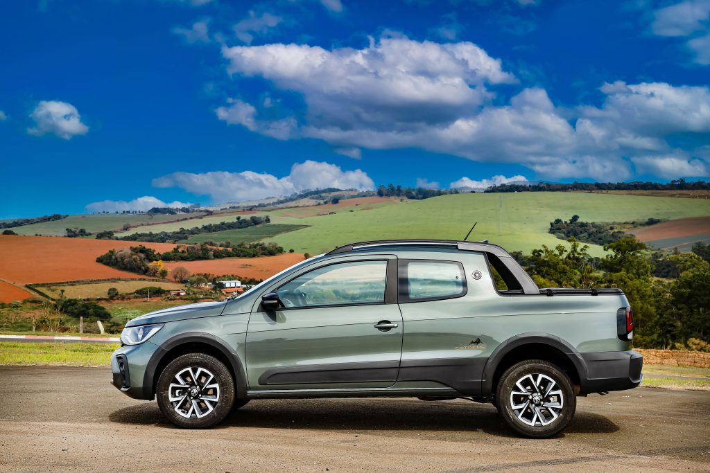 Volkswagen Saveiro vista de lado em ambiente rural bucólico, cercada por vegetação e cenário campestre.