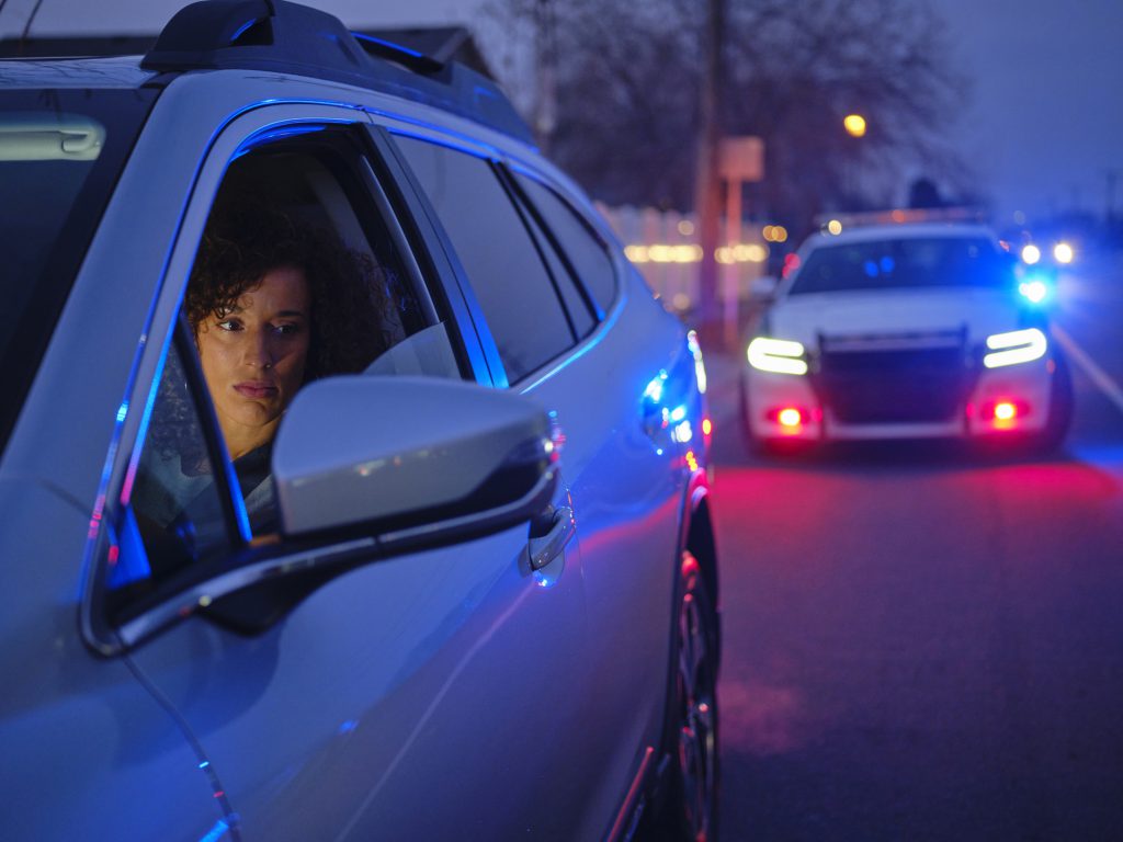 A young multiracial woman in a car, pulled over by a police officer at night.