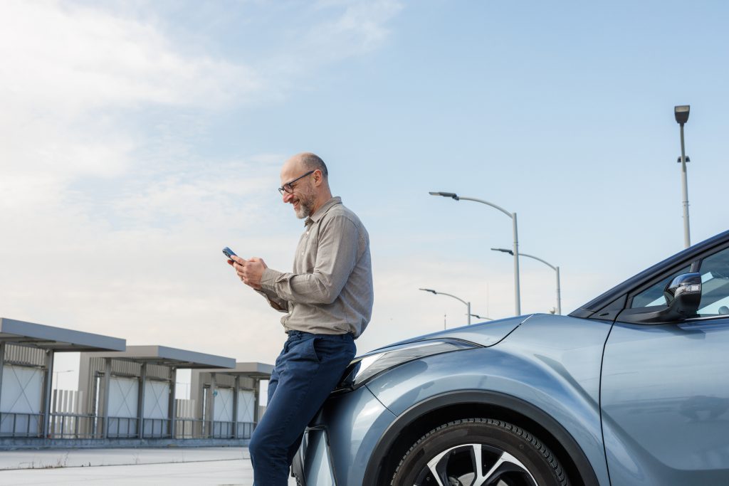 A stylish man in a beige shirt and glasses smiles while looking at his phone, symbolizing technology and success.