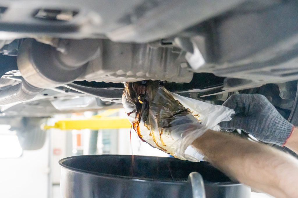 A mechanic drains a car's used engine oil
