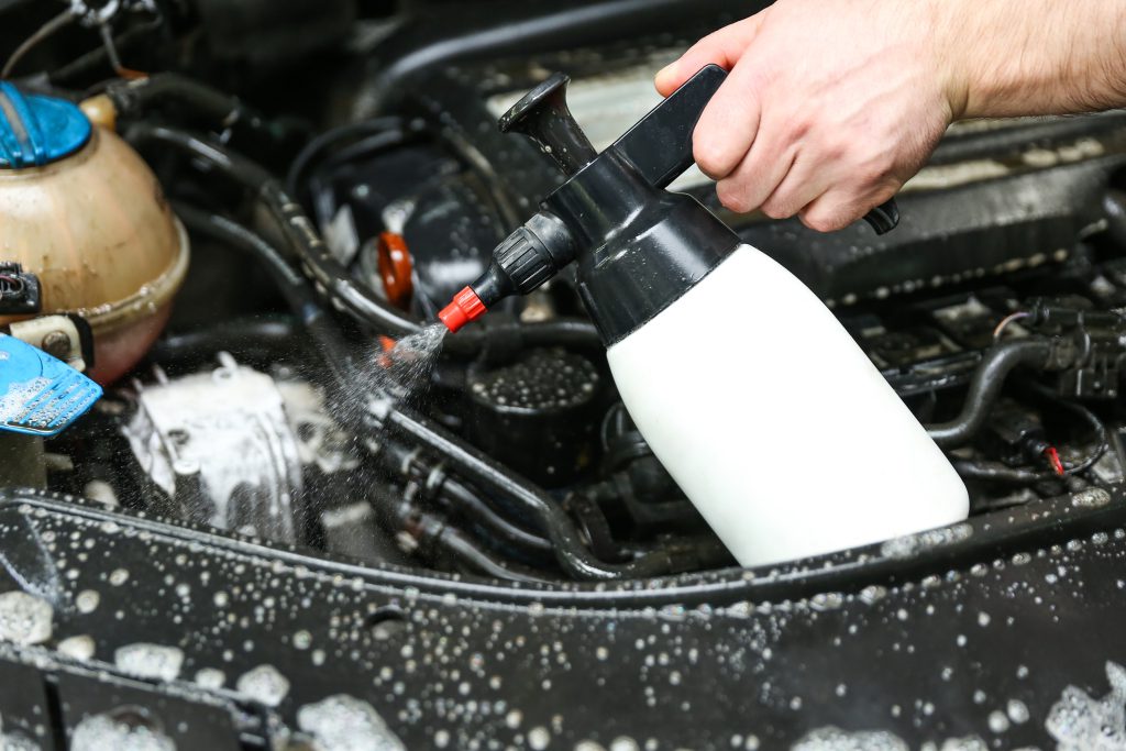Pessoa aplicando espuma para lavar o carro, cobrindo a lataria com produtos de limpeza automotiva.