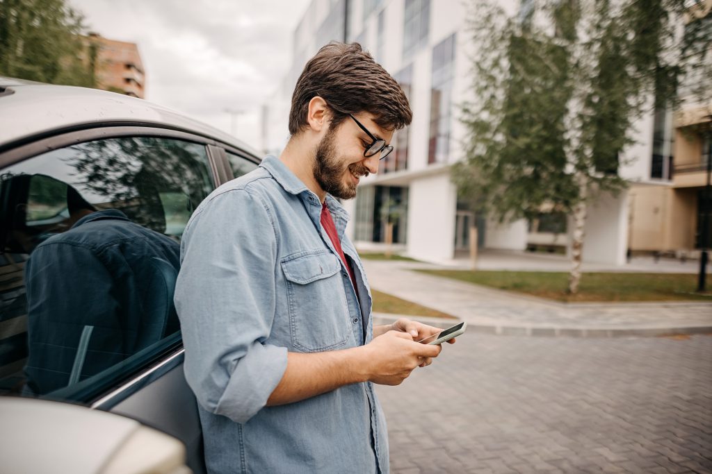 Young man using phone in front of the car
