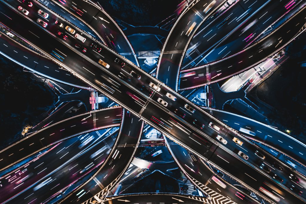 Imagem noturna de estradas entrecruzadas com vários carros em movimento e iluminação destacando o trajeto.