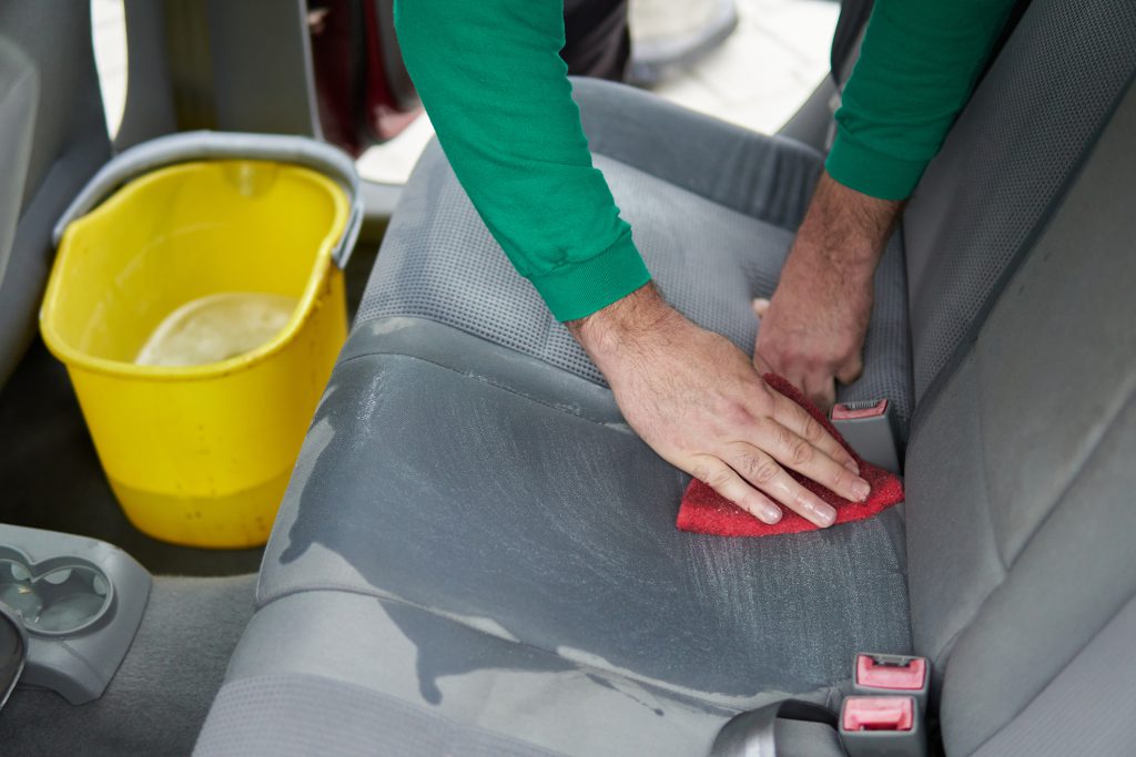 Car cleaning detailing - male using professional steam vacuum chemical cleaning for dirty car interior seats with extraction method