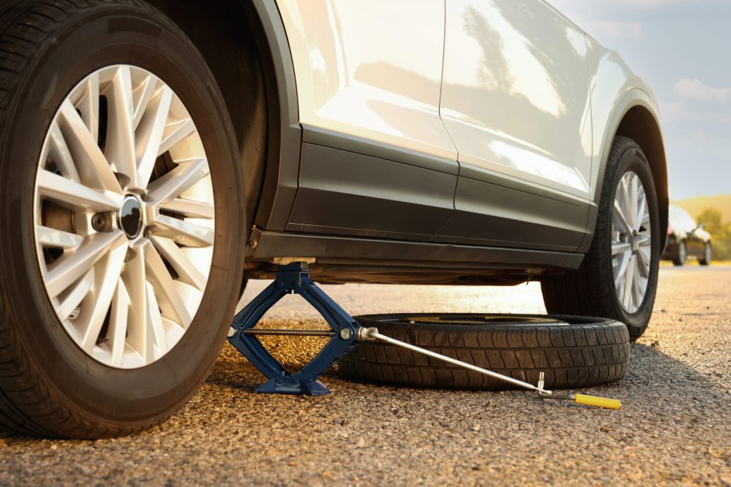 Car lifted by scissor jack and spare wheel on roadside