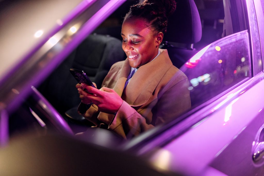 Mulher dentro do carro com luzes roxas no interior usa o celular, destacando a conectividade e as atualizações OTA do veículo.