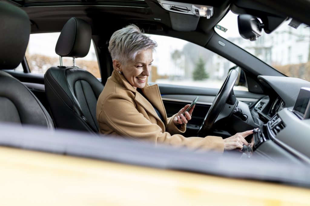 mulher de cabelos brancos, elegante, conectando seu celular ao wi-fi do carro, interior moderno e iluminado