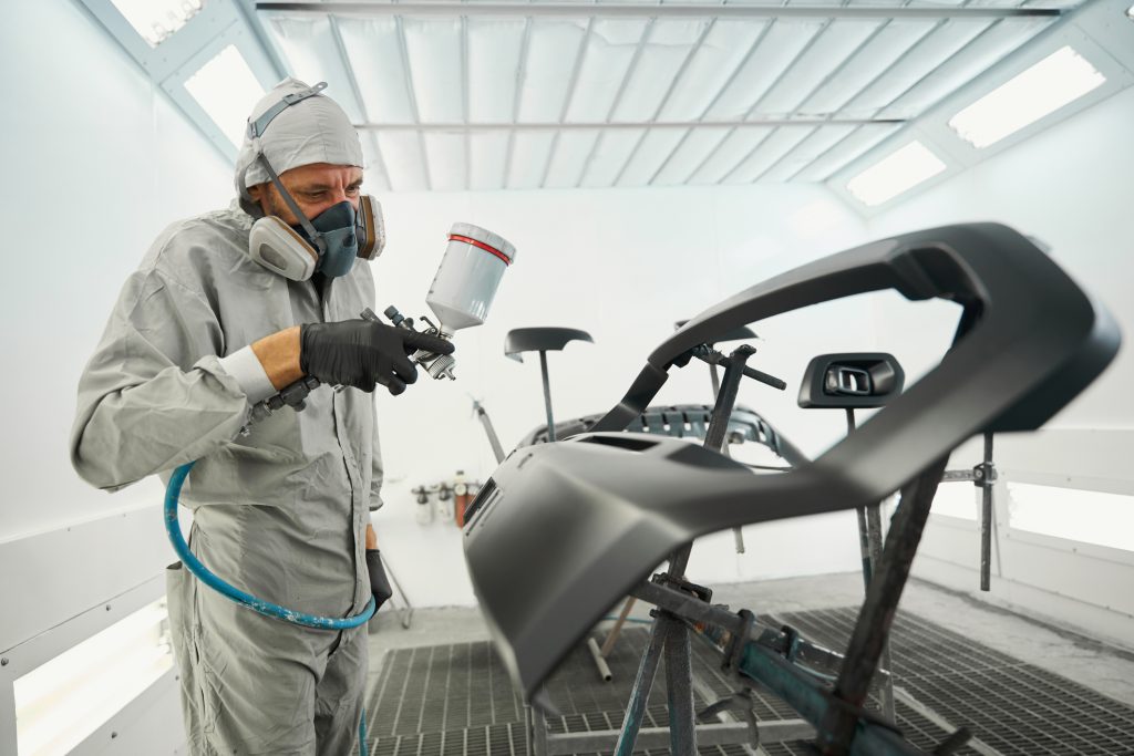 profissional com equipamento de proteção aplicando nova camada de tinta na lataria do carro