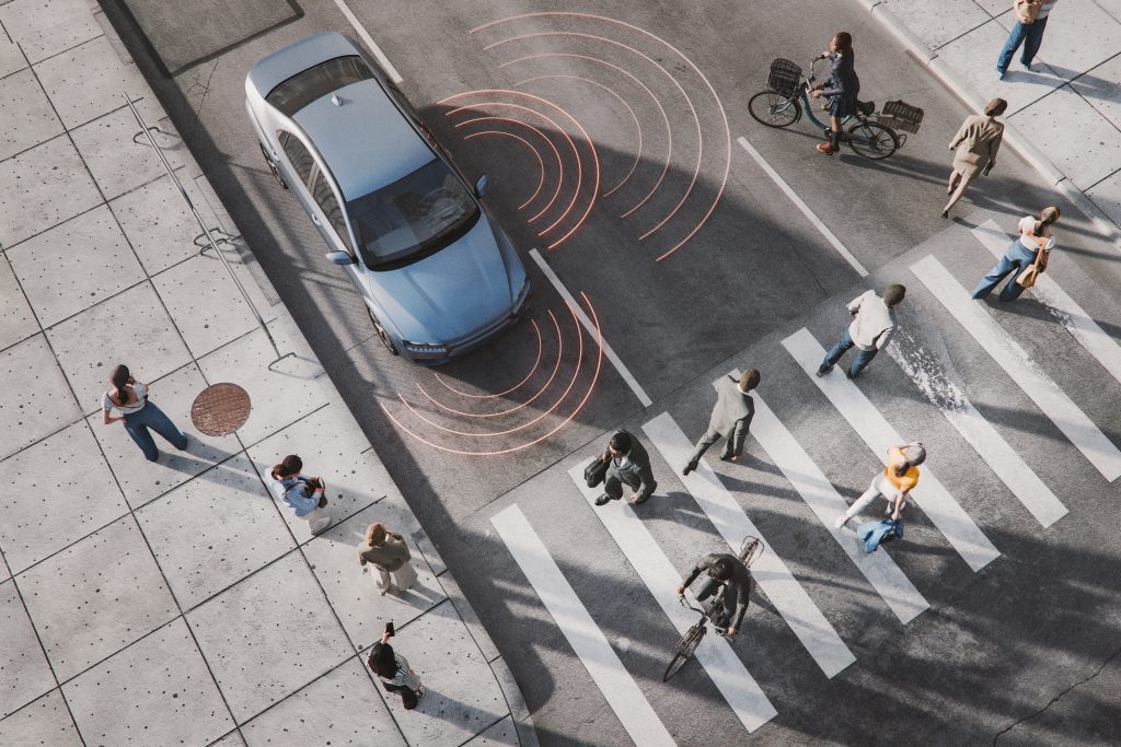 Imagem 3D computadorizada de um carro com sensores detectando pessoas atravessando a rua, representando tecnologia automotiva e segurança.