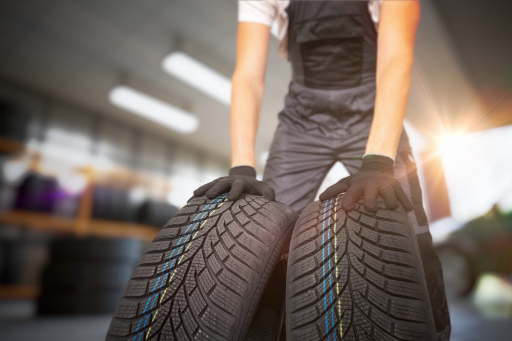 homem com luvas segurando dois pneus dentro de uma oficina automotiva