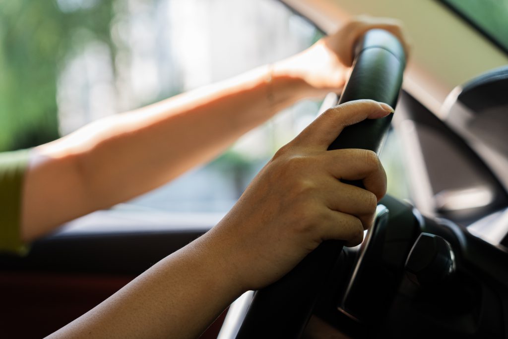 Pessoa com a mão no volante, detalhe em foco no sistema de direção hidráulica do carro.