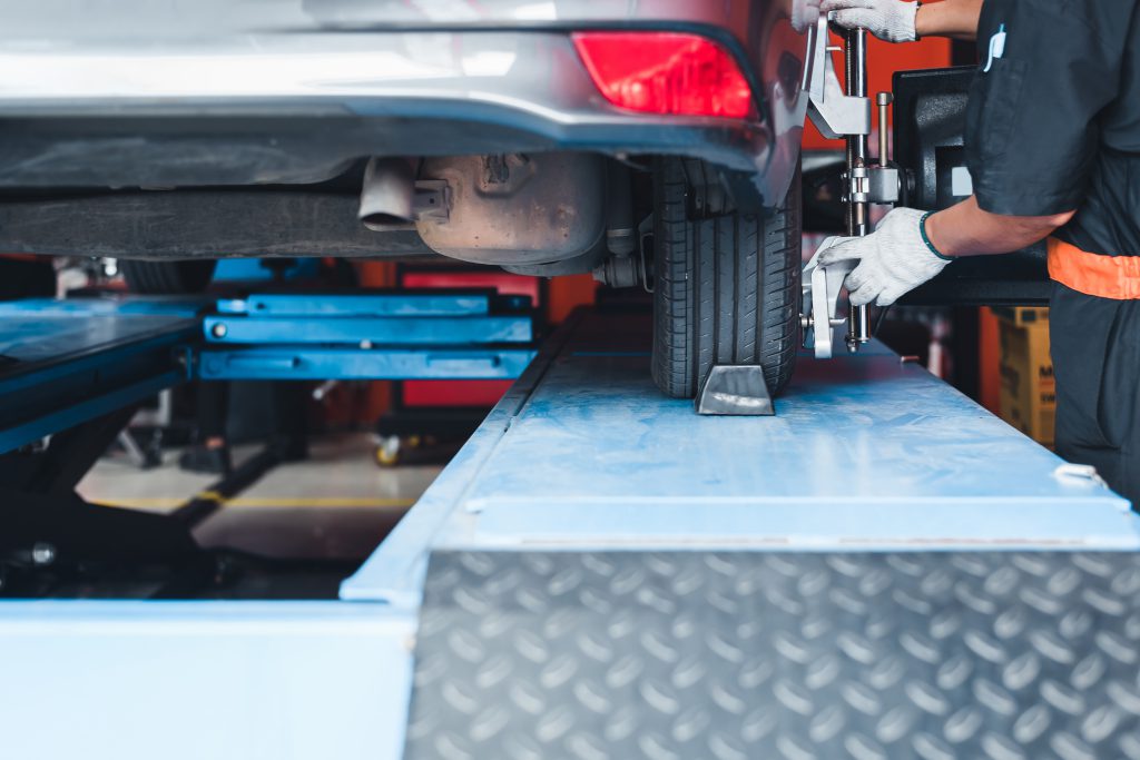 In the service station workshop, a car is on a stand with sensors on the wheels being checked for wheel alignment and camber.