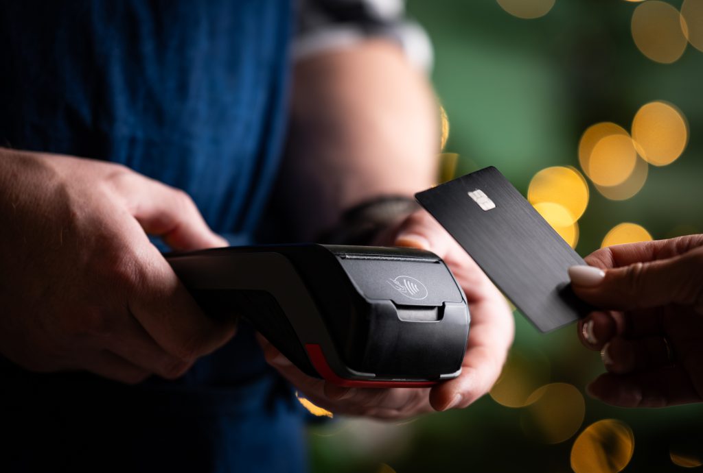 Female Hand Pays By Card On A Pos Terminal Against A Blurred Christmas Background
