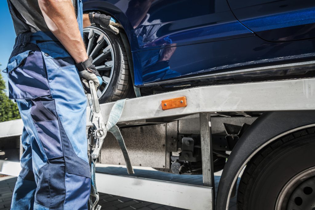 Male Worker Putting Transport Belts Around the Wheel of a Car on His Trailer to Secure It for Safe Carriage. Vehicle Transportation Theme.