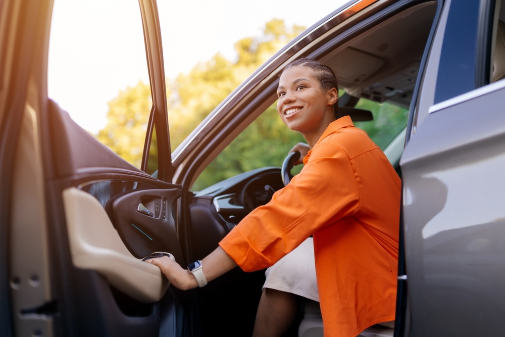 Mulher no banco do motorista, com a porta aberta, sorrindo.